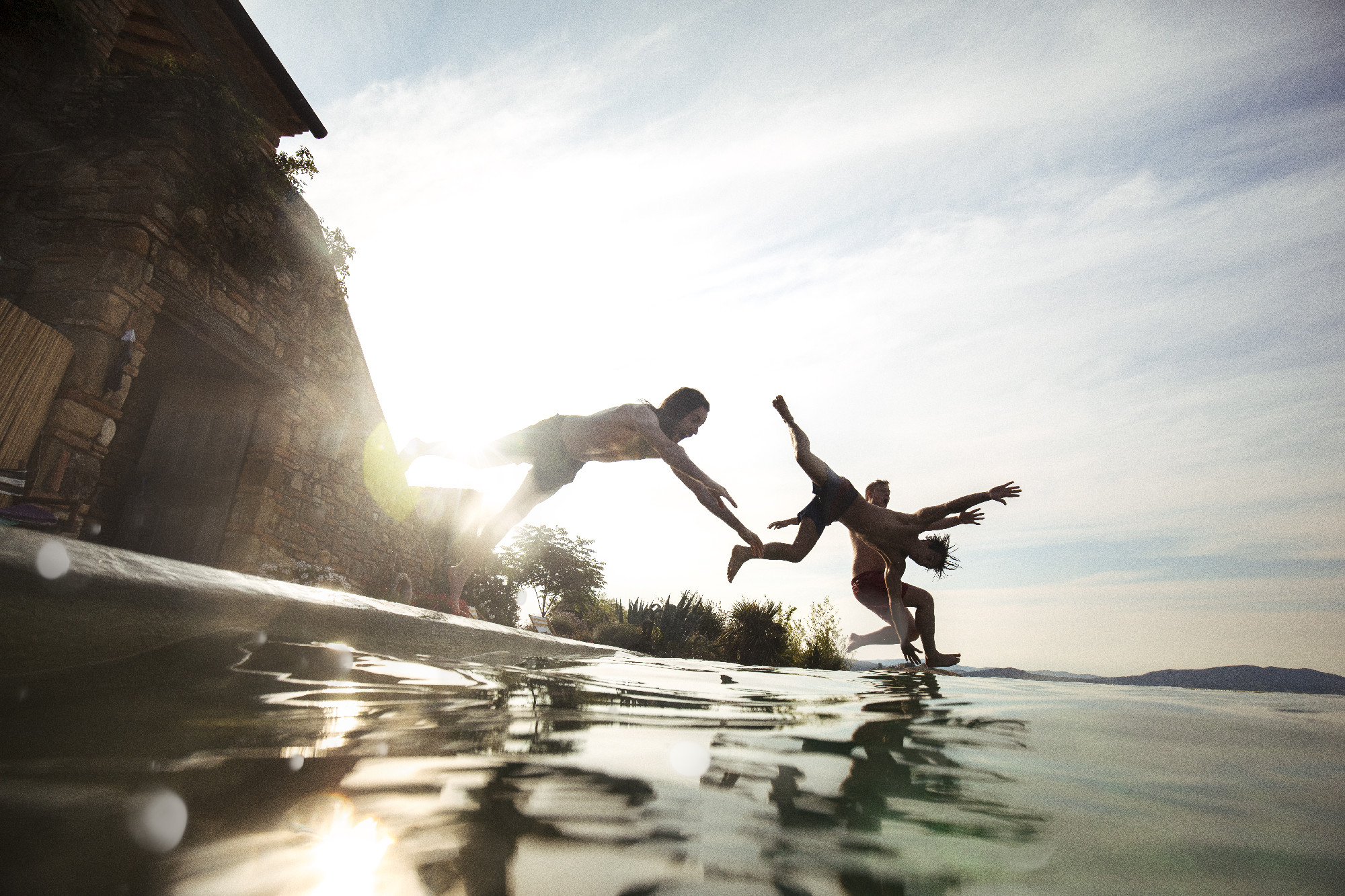Tre persone si tuffano in piscina al tramonto, sprigionando gioia e libertà.